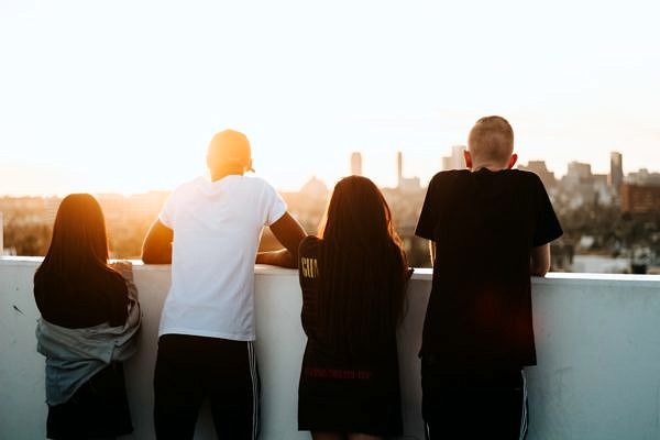 A group of four teenagers stand watching a sunset over a low concrete wall