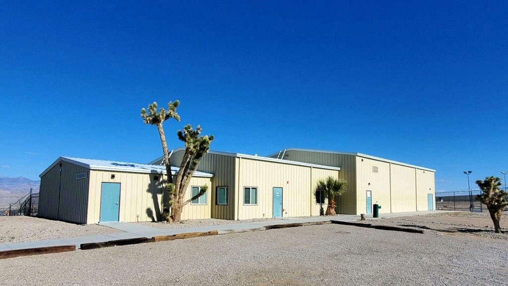 A long building surrounded by a few trees, desert, and a clear sky