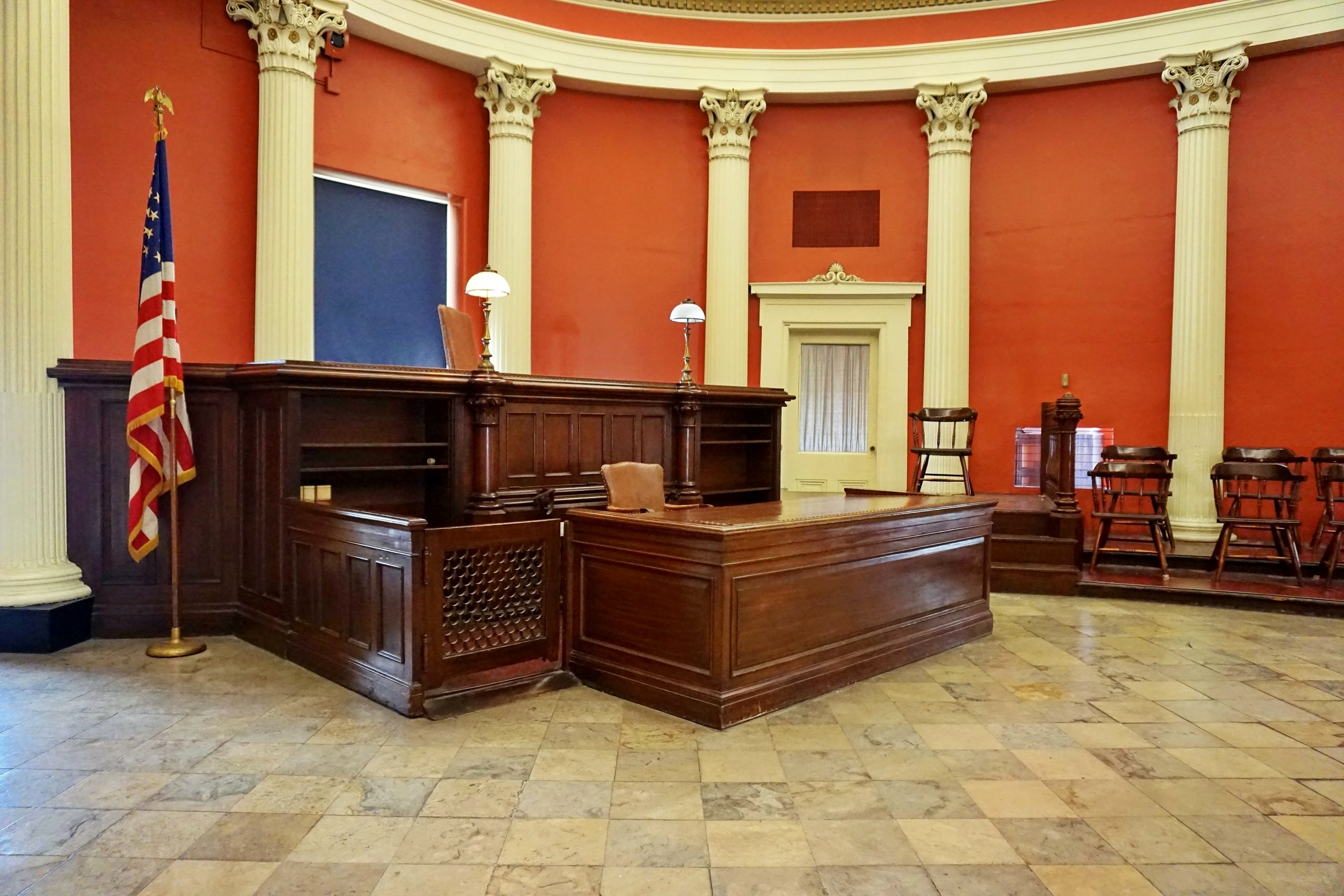 A photo of an empty courtroom showing the judge's bench, a witness stand, and the jury box