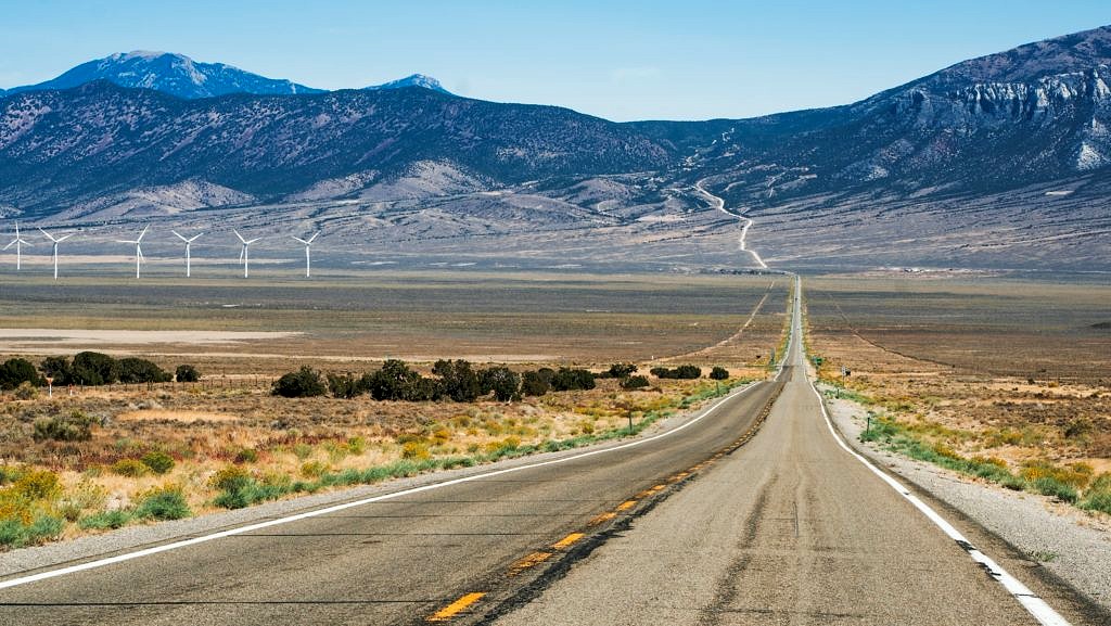 A two-lane road runs through the Nevada desert with mountains in the distance