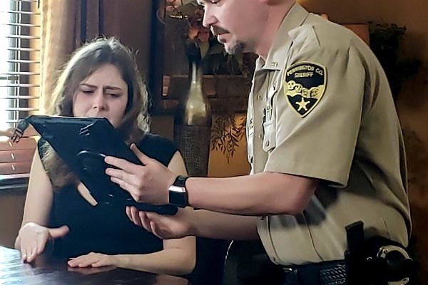 A sheriff's deputy shows an iPad screen to a woman sitting at a table in a demonstration of South Dakota's Virtual Crisis Care program