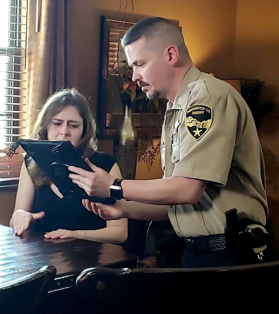 A sheriff's deputy shows an iPad screen to a woman sitting at a table in a demonstration of South Dakota's Virtual Crisis Care program