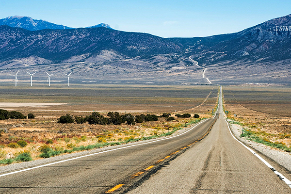 A two-lane road runs through the Nevada desert with mountains in the distance