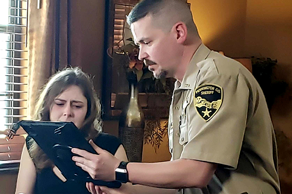 A sheriff's deputy shows an iPad screen to a woman sitting at a table in a demonstration of South Dakota's Virtual