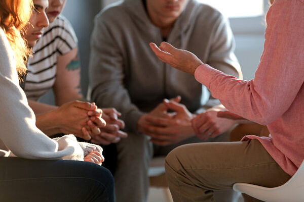 Close-up of a person gesticulating while talking to a group of people during a meeting.